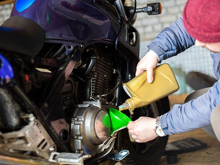 Man pouring engine oil from a gold bottle into a blue motorcycle sportsbike