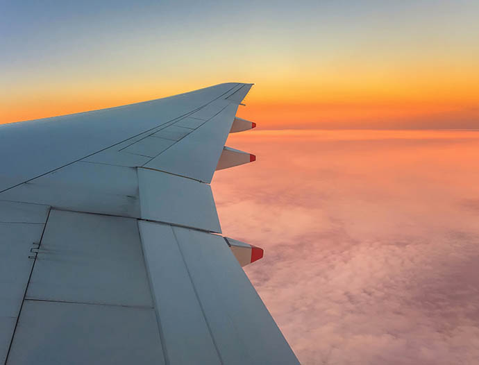 View of an airplane wing in flight over sunset clouds