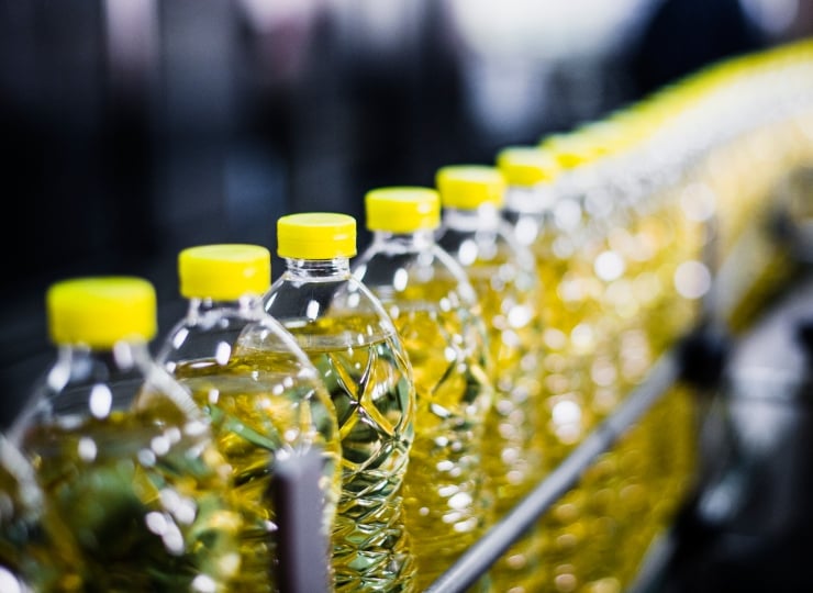 Bottles of oil moving along a conveyor belt, emphasizing the significance of food contact testing for packaging materials